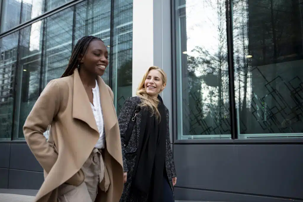 Deux professionnelles marchant et échangeant devant un immeuble de bureaux vitré