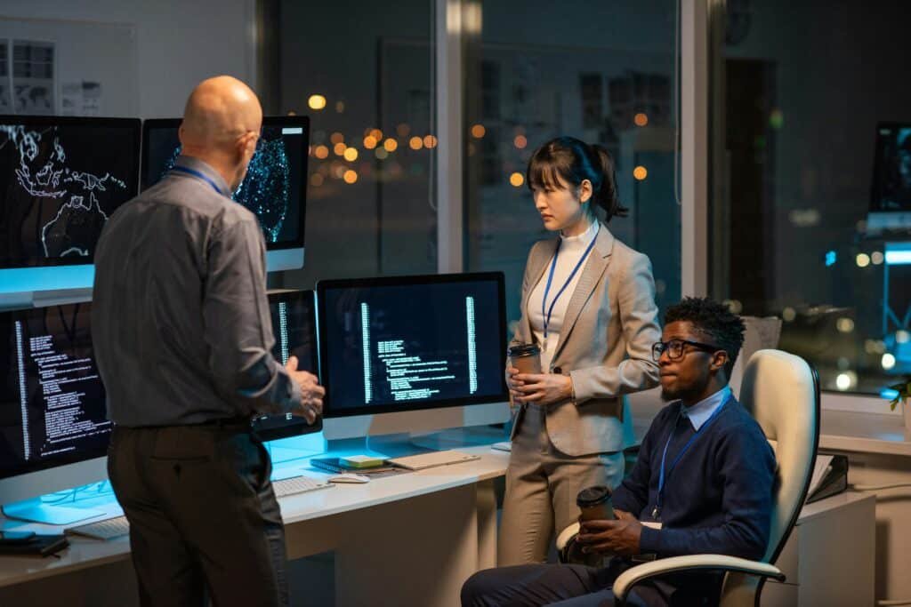 Equipe technique analysant des tableaux de bord de donnees sur plusieurs ecrans dans le cadre d'un projet de migration de systeme d'information